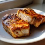 Two thick, juicy baked pork chops oven boneless, seasoned and browned, resting on a white plate.