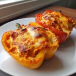 Two halves of keto buffalo chicken stuffed peppers, baked with a bubbly, browned cheese topping, served on a white plate.