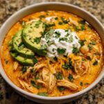 A close-up of a bowl of creamy keto chicken taco soup topped with avocado slices, sour cream, and cilantro.