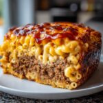 A thick slice of baked mac and cheese meatloaf casserole showing layers of seasoned ground meat and creamy macaroni.