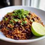 Close-up of a white bowl filled with Mexican black beans and rice recipe, topped with fresh cilantro and a lime wedge.