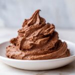 A generous swirl of rich, dark milk chocolate buttercream frosting piled high in a white bowl.