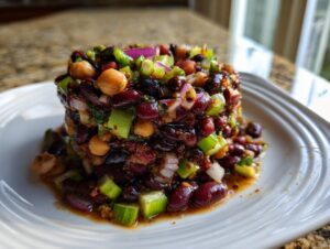 A molded, cylindrical serving of dense bean salad featuring kidney beans, chickpeas, celery, and red onion.