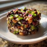 A molded serving of dense bean salad featuring black beans, chickpeas, red onion, and green onions on a white plate.
