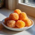 A pile of bright orange cream cheese mints rolled in coarse sugar, sitting on a small white plate.