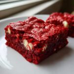 A close-up shot of a rich, vibrant red velvet cake mix cookie bars square featuring visible white chocolate chips.