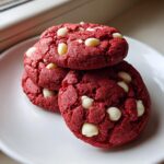 A stack of four vibrant red velvet cake mix cookies with white chocolate chips resting on a white plate.