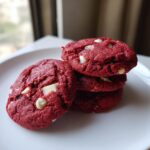 A stack of four vibrant red velvet cake mix cookies studded with white chocolate chips, resting on a white plate.