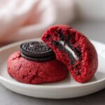 Close-up of vibrant red velvet cake mix cookies with Oreos, one cookie is broken open showing the creamy filling.