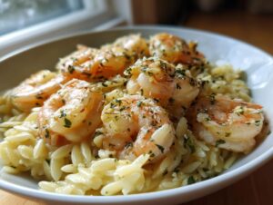 A close-up of a white bowl filled with creamy shrimp orzo pasta, topped with seasoned, cooked shrimp and fresh parsley.