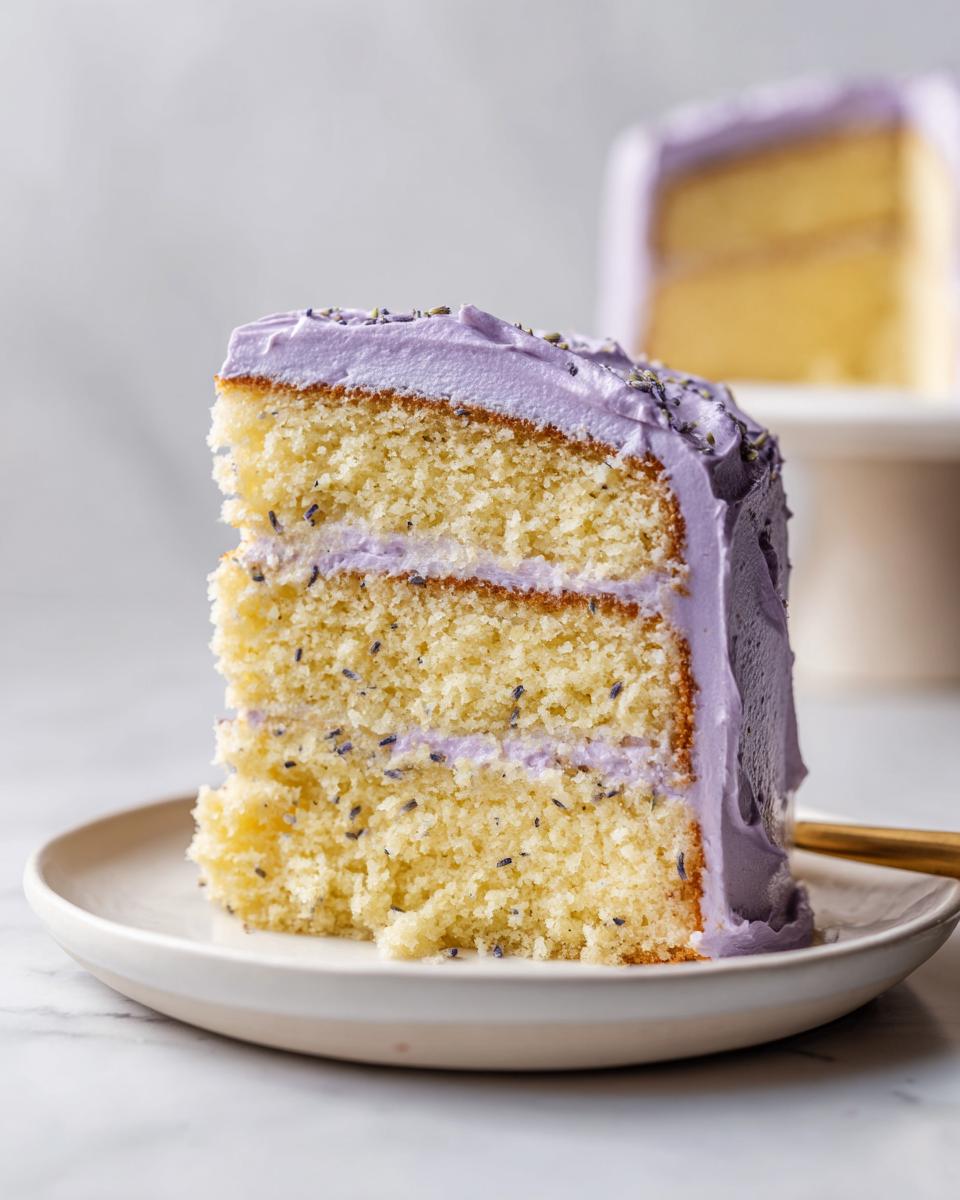 Close-up of a moist slice of lavender cake showing two layers and light purple lavender frosting.
