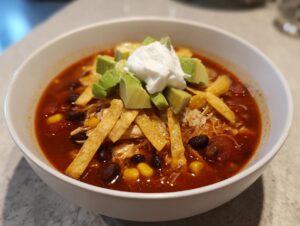 A vibrant bowl of slow cooker chicken tortilla soup topped with avocado, sour cream, and tortilla strips.