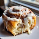 Close-up of a soft gluten free cinnamon rolls recipe roll dripping with thick white icing.