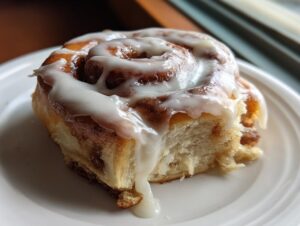 A close-up of a single, soft gluten free cinnamon rolls recipe serving, generously topped with dripping white icing.