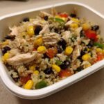 Close-up of a southwest salad meal prep featuring shredded chicken, quinoa, corn, black beans, and diced peppers in a white container.