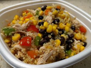 Close-up of a portable container filled with a southwest salad meal prep mix featuring quinoa, shredded chicken, corn, and black beans.