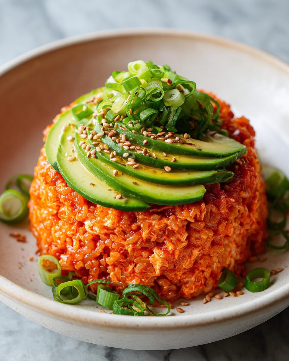 Close-up of a perfectly molded spicy crab sushi bowl topped with sliced avocado, sesame seeds, and chopped green onions.