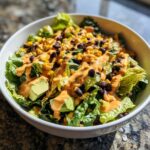A vibrant bowl of spicy southwest salad topped with black beans, corn, avocado, and a creamy orange dressing.