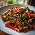 A close-up, appetizing shot of street style thai drunken noodles with chicken, wide rice noodles, and red peppers.