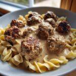 Close-up of savory Swedish meatballs smothered in creamy brown gravy served over egg noodles.