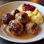 Close-up of four juicy swedish meatballs with frozen meatballs gravy, mashed potatoes, and lingonberry jam.