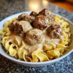 A close-up of savory swedish meatballs over egg noodles smothered in creamy gravy.