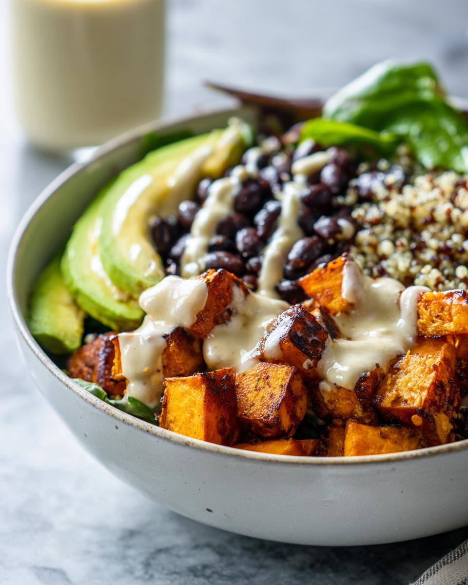 Close-up of a sweet potato buddha bowl featuring roasted sweet potatoes, black beans, quinoa, avocado, and creamy dressing.