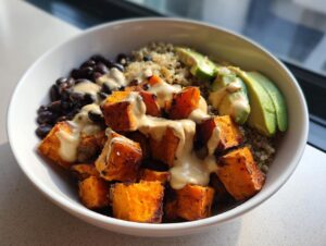 Close-up of a delicious sweet potato buddha bowl featuring roasted sweet potatoes, black beans, quinoa, avocado, and creamy dressing.