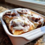 Four freshly baked and generously iced tiktok cinnamon rolls recipe in a white baking dish.