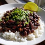 A close-up of a bowl of ultimate black beans and rice topped with fresh cilantro and a lime wedge.