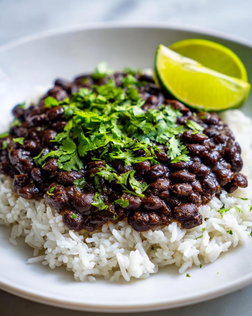 Close-up of a bowl featuring fluffy white rice topped with rich black beans and fresh cilantro, garnished with a lime wedge.