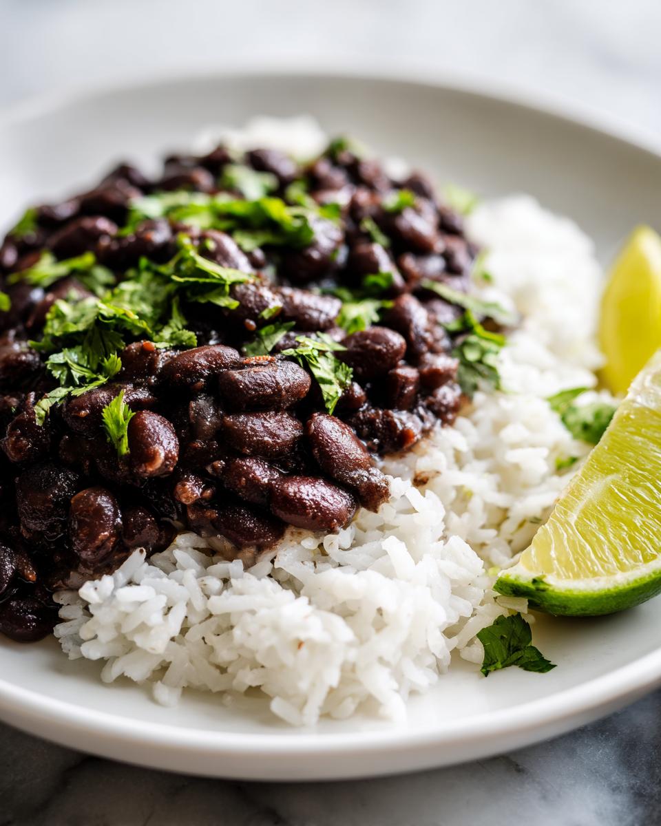 Close-up of a white bowl filled with fluffy white rice topped generously with seasoned black beans and fresh cilantro, served with a lime wedge.
