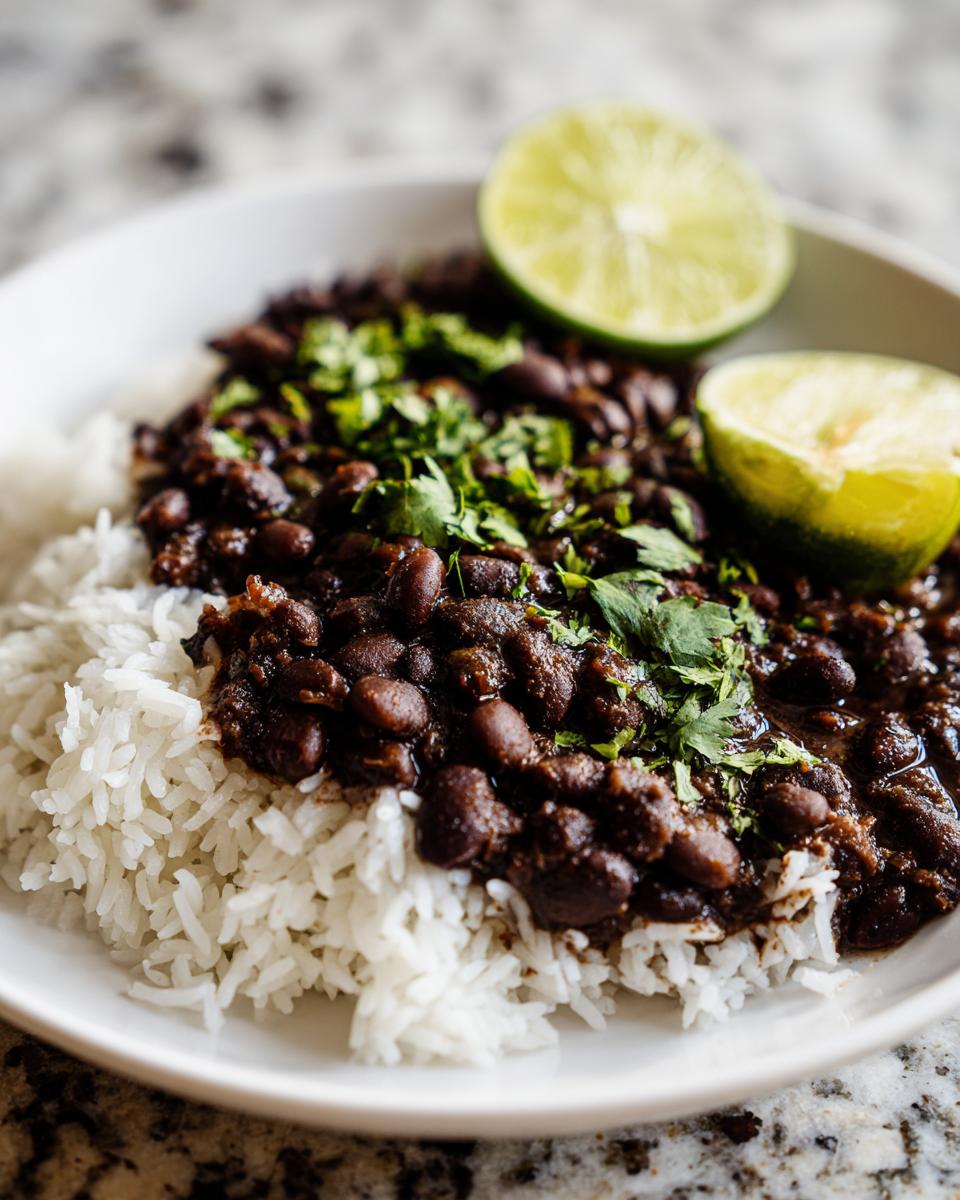 Close-up of a white bowl filled with white rice topped generously with seasoned black beans and fresh cilantro, garnished with lime wedges.