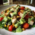 Close-up of a vibrant Southwest salad topped with grilled chicken, corn, black beans, tomatoes, and creamy green dressing.