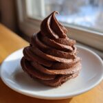 A tall, perfectly piped swirl of rich, dark whipped chocolate buttercream frosting on a white plate.