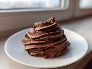 A beautiful swirl of rich, dark whipped chocolate buttercream frosting piped onto a small white plate.