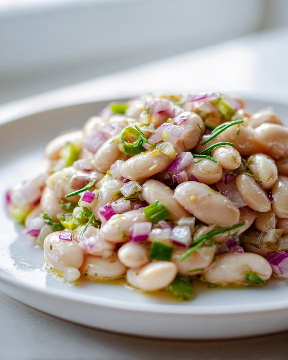 A close-up serving of bright white bean salad mixed with diced red onion, green herbs, and a light vinaigrette.
