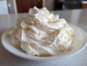 A generous swirl of fluffy white chocolate buttercream frosting piped high in a small white bowl.