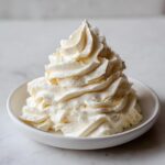 A tall, beautifully piped swirl of creamy white chocolate buttercream frosting in a small white bowl.