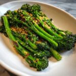 Close-up of bright green, roasted broccolini stalks topped with toasted garlic and seasoning.