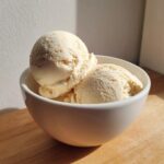 Two scoops of creamy, light yellow cottage cheese ice cream served in a white bowl.