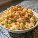 Close-up of a bowl filled with creamy deviled egg pasta salad, topped generously with bright red paprika.