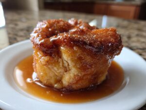 Close-up of a single, golden-brown apple dumpling covered in thick caramel sauce on a white plate.