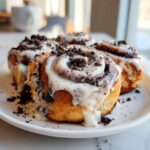 Close-up of several gooey Oreo cinnamon rolls topped with white icing and crushed cookie pieces.