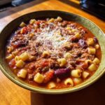 A close-up of a rich, tomato-based pasta e fagioli soup topped with grated Parmesan cheese.