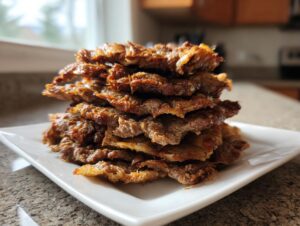 A tall stack of thinly sliced, crispy, browned meat, resembling homemade doner kebab, served on a white square plate.