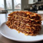 A tall stack of layered flatbread filled with seasoned ground meat, resembling homemade doner kebab, served on a white plate.